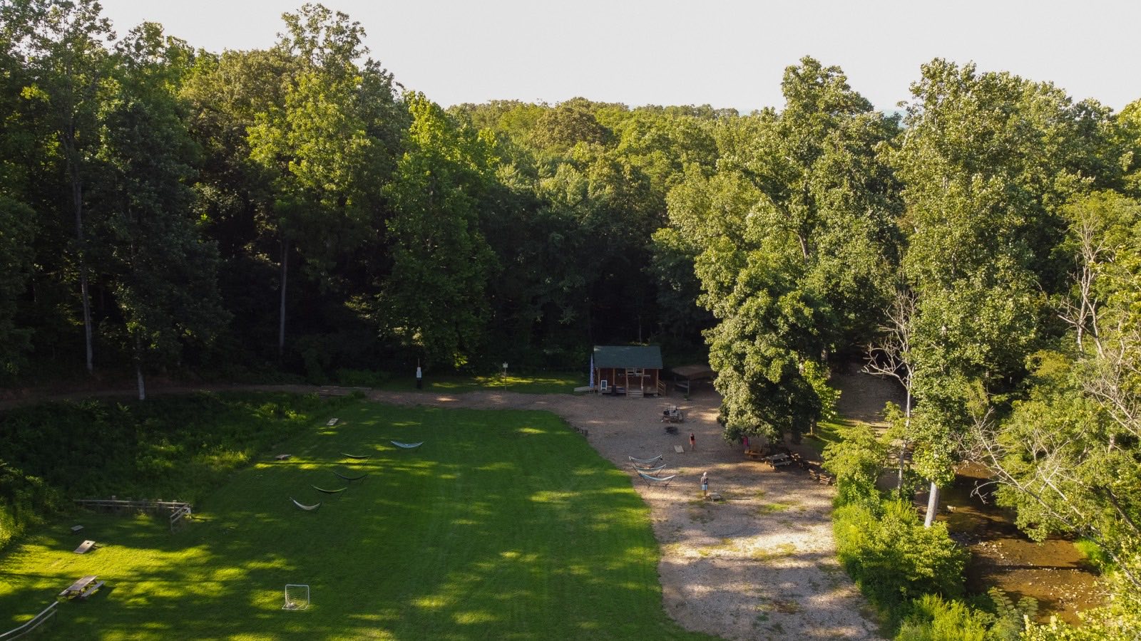Aerial view of the meadow at Brewing Tree — hammocks and yard games on the grass, the river bar, and the North Fork of the Rockfish River running along the tree line