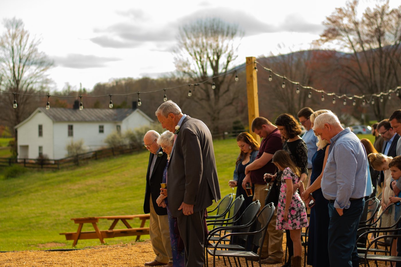 Wedding guests gather under string lights with the mountains behind